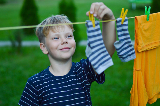 一个快乐的9岁白人男孩帮助她的妈妈挂衣服。通过家庭活动发展精细运动技能。有选择性的重点。图片下载