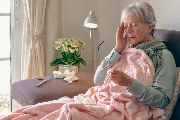 老年白人妇女躺在家里的沙发上，有头痛和发烧的症状，如季节性流感或冠状病毒图片下载