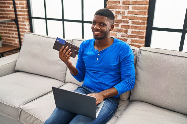 年轻的非裔美国人用笔记本电脑和信用卡坐在家里的沙发上图片下载