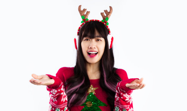 年轻的亚洲妇女在红色毛衣戴耳罩和驯鹿角头带摆姿势在白色背景。圣诞快乐。图片下载