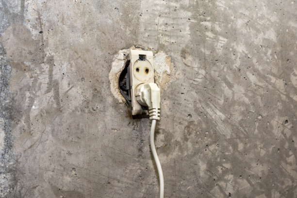 旧混凝土墙上一个烧坏的插座和一个电插头图片下载
