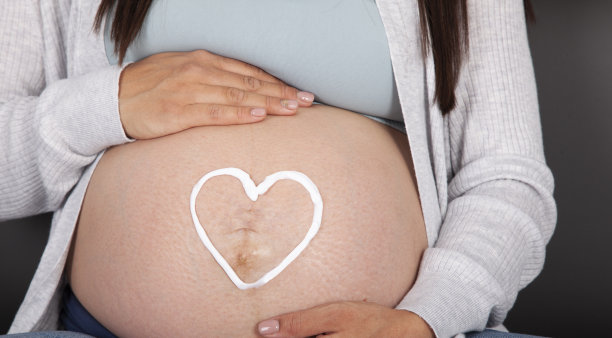 特写的孕妇与身体乳液心形腹部图片下载