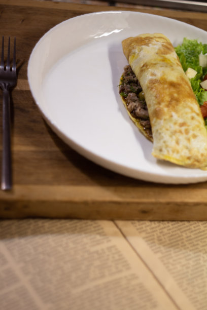 金枪鱼煎饼和沙拉放在白色盘子上，木砧板上有叉子，放在旧报纸上——垂直照片图片下载