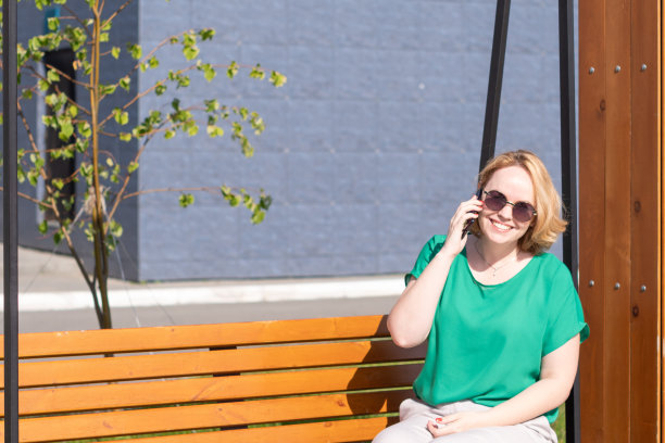 一个戴着墨镜的微笑的女人，和朋友们在电话里聊天，在夏天的公园里约会。图片下载