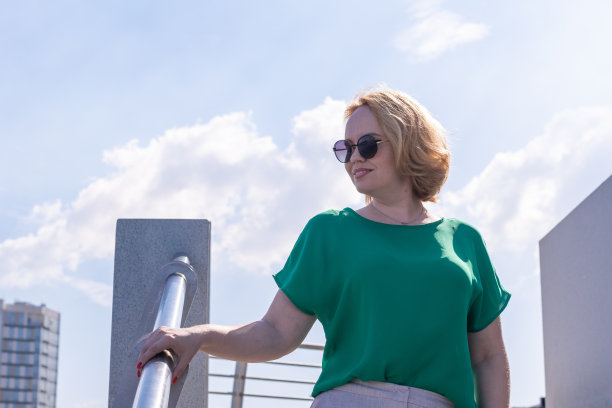 画像一个微笑快乐的中年妇女戴着太阳镜，绿色衬衫站在河岸。图片下载