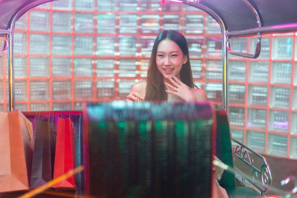 工作室的肖像照片，一个美丽的年轻的亚洲女性模特穿着连衣裙与许多红色和棕色的纸购物袋摆姿势快乐地坐在曼谷的一辆嘟嘟出租车图片下载