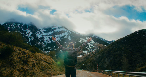 度假旅行的男人走在山路上，高举双手享受自由图片下载