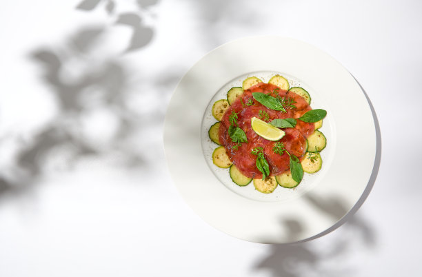 牛肉肉片配西葫芦和黄瓜放在阳光阴影的白色桌子上。夏季餐桌上的开胃菜——牛肉肉片。意大利风味的生肉片。审美菜单。图片下载