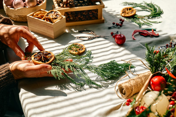 一名妇女用冷杉树枝和干橙子做圣诞安排。女性的双手创造了圣诞手工艺手工装饰。庆祝新年。冬天的假期。图片下载