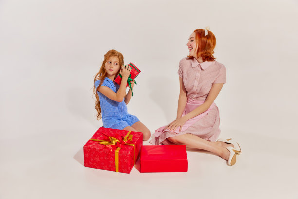 美丽的女人和小女孩的肖像，孩子颤抖的礼物盒子近耳朵孤立的灰色背景。寒假图片下载