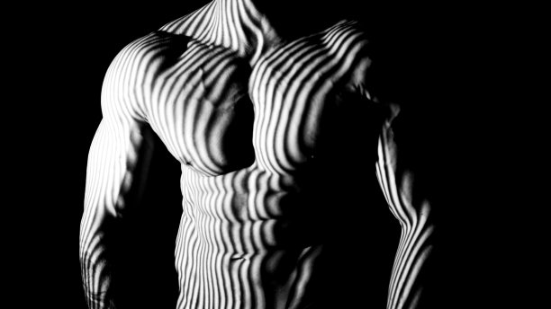 特写灰度肌肉男展示肌肉的胸部摆姿势的相机与抽象的灯光效果在黑色背景图片下载