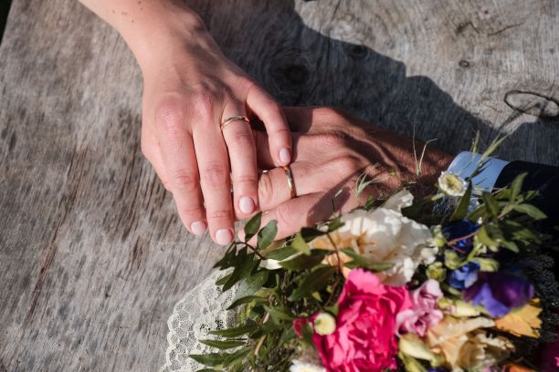 新娘和新郎的手与结婚戒指和花束放在木表面图片下载