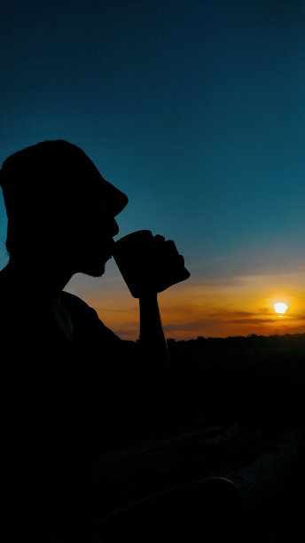 一个男人在夕阳下从杯子里喝水的剪影图片下载
