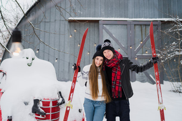 一对快乐的情侣穿着温暖舒适的衣服，在花园里抱着滑雪板。图片下载