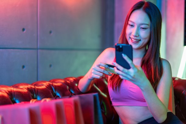 肖像照片的年轻美丽的亚洲女模特在霓虹灯的房间进行支付与她的信用卡借记卡在她的手机后购物狂欢图片下载
