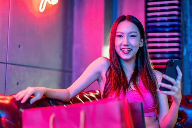 肖像照片的年轻美丽的亚洲女模特在霓虹灯房间聊天愉快的她的手机购物狂欢后图片下载