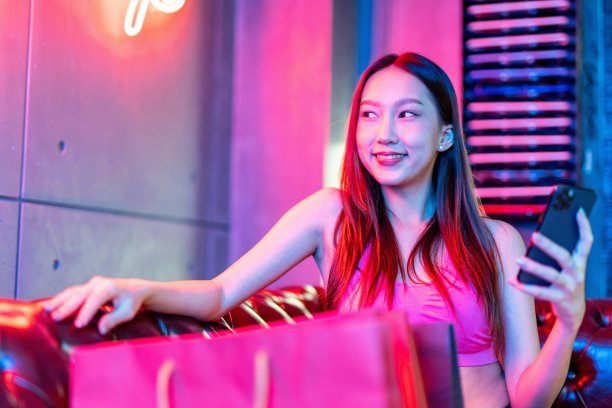 肖像照片的年轻美丽的亚洲女模特在霓虹灯房间聊天愉快的她的手机购物狂欢后图片下载