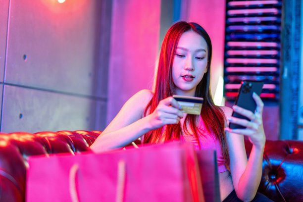 肖像照片的年轻美丽的亚洲女模特在霓虹灯的房间进行支付与她的信用卡借记卡在她的手机后购物狂欢图片下载
