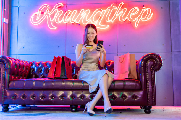 肖像照片的年轻美丽的亚洲女模特穿着优雅的衣服在霓虹灯的房间支付与她的信用卡借记卡在她的手机网上购物狂欢图片下载