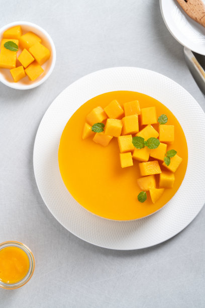 美味的釉面芒果无烤芝士蛋糕与新鲜的芒果果肉丁顶在明亮的桌子背景。图片下载