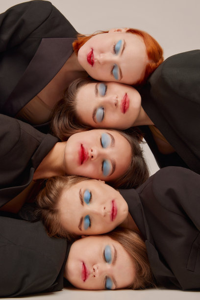 年轻美丽的女性在黑色夹克与明亮的妆容，红色的口红蓝色的眼影摆姿势，躺在头在灰色的背景图片下载