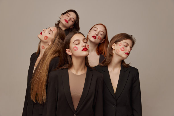 在灰色背景下，年轻美丽的女性穿着黑色夹克，涂着红色口红，闭着眼睛摆姿势。吻痕图片下载