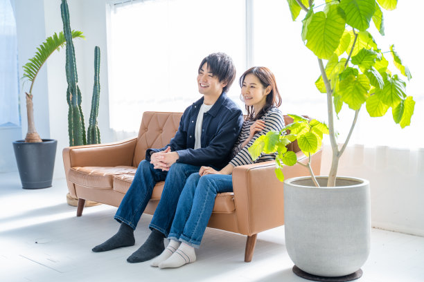 一对微笑的夫妇坐在沙发上，客厅里有明亮的树叶。图片下载