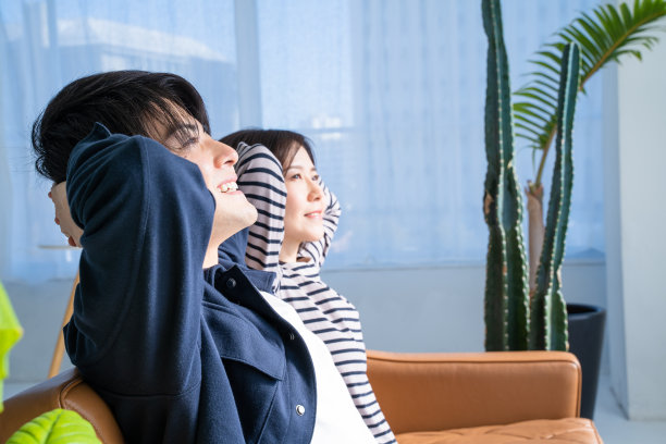 一对夫妇的侧面坐在沙发上，依偎在客厅明亮的树叶植物上图片下载