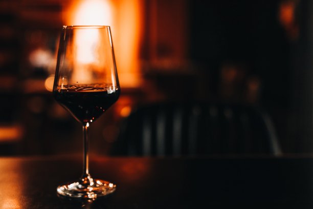 在黄昏的光线中，木桌上放着一杯深红色的葡萄酒图片下载