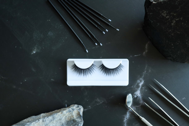 睫毛延伸工具在时髦的黑色背景和石头。假睫毛，镊子和刷子。美容沙龙。妆化妆品。俯视图，平铺图片下载