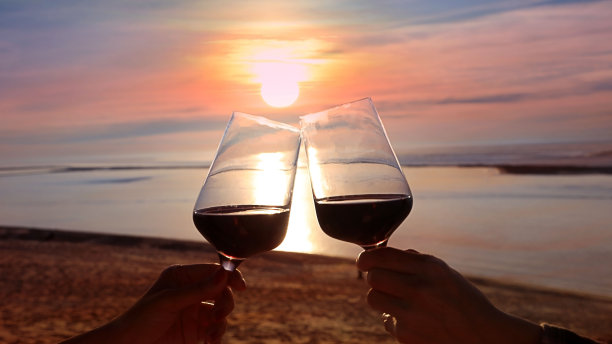 剪影浪漫的夫妇彼此敬酒，坐在一起在沙滩上的日落场景心情图片下载