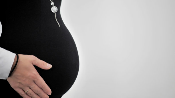 侧面的一个孕妇，她的手在她的肚子上。孤立的白色背景。图片下载