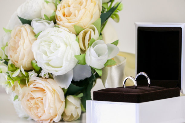 一对精致闪亮的他/她的结婚戒指在戒指盒闪闪发光，除了漂亮的婚礼花花束，白色和桃红色的玫瑰。爱情、浪漫和婚姻的象征。图片下载