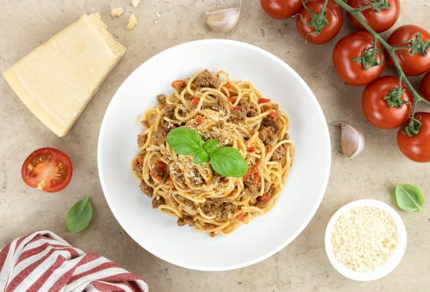 意大利肉酱面配鲜罗勒、番茄、大蒜和帕尔马干酪，米色背景。白色盘子里的炖牛肉酱意大利面，俯视图。传统的意大利食物。图片下载