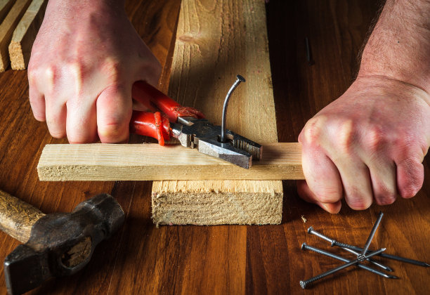 工人用钳子把弯曲的钉子从板上拔出来。木工手特写。车间的工作环境图片下载