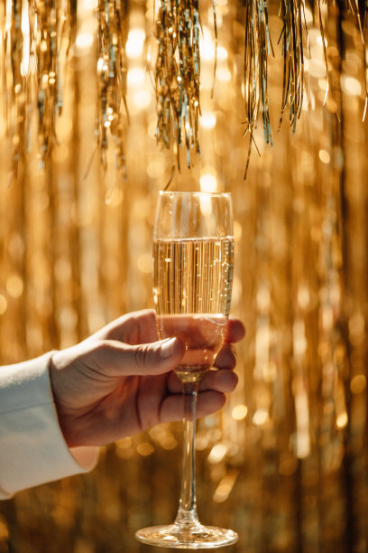 男士手中的香槟杯映衬着奢华的霞光金雨装饰奢华的假日派对图片下载