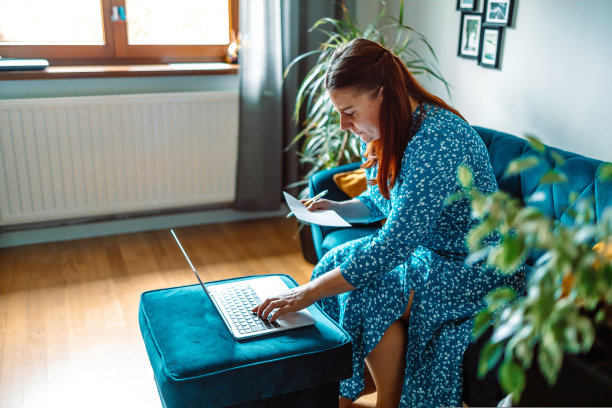 美丽严肃的女人用笔记本电脑支付账单，而坐在家里的房间沙发上图片下载