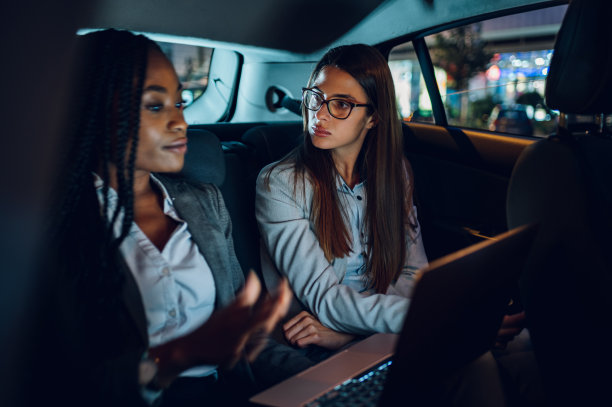 两个多种族的女商人开着车，用着笔记本电脑图片下载