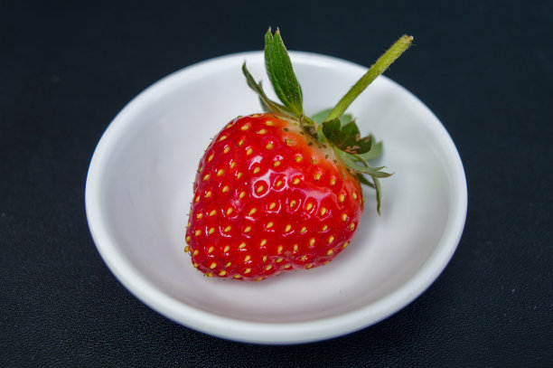 新鲜草莓在白色杯子隔离在黑色背景。图片下载