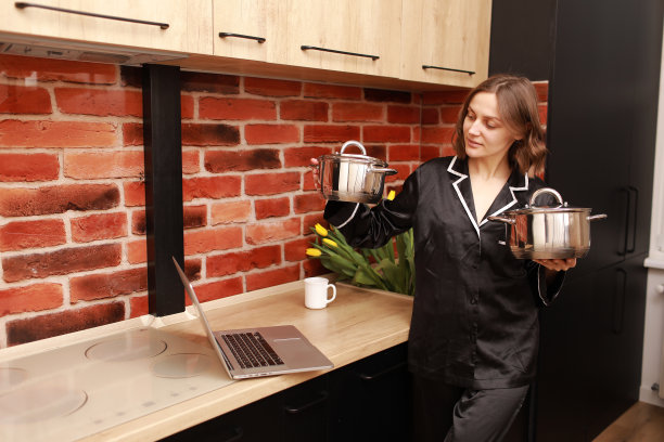 在线烹饪教程。裁剪的照片手的女人女孩用笔记本电脑进行视频博客，在现代厨房里拿着平底锅图片下载