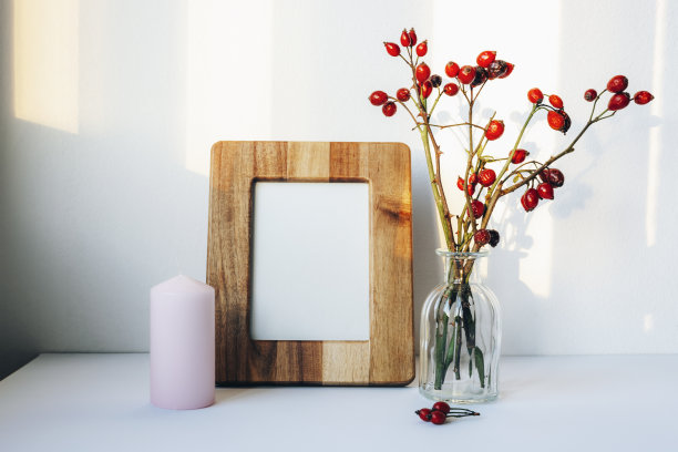 空白相框，蜡烛和玫瑰玫瑰枝花瓶在白色的桌子。前视图，模拟图片下载