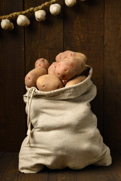 装满土豆和大蒜的袋子，在深色的木头背景下编成花环图片下载