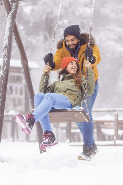 在雪天的户外秋千上，男朋友推着女朋友图片下载