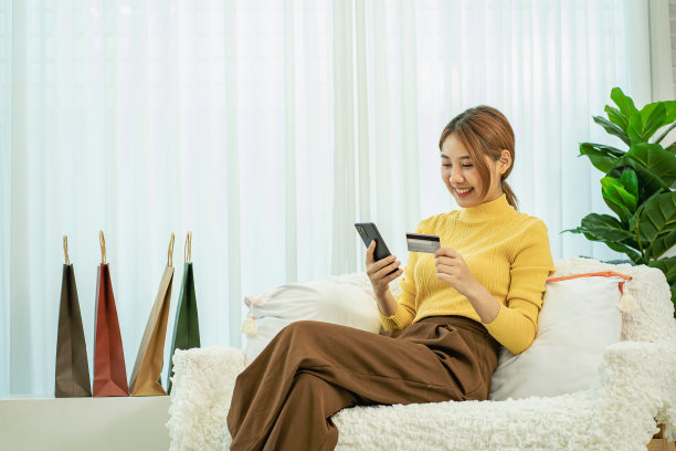 电子商店的概念，年轻微笑的亚洲妇女手持信用卡使用智能手机支付在线，家庭购物，电子商务，网上银行，图片下载