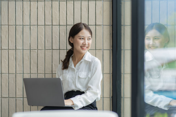迷人的亚洲女子独自坐在咖啡馆的桌子旁，她看起来像是在看着自己的笔记本电脑工作，微笑着，工作在线的概念。图片下载