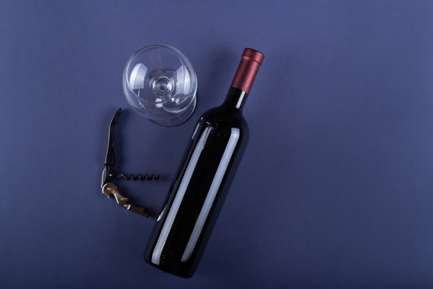 红色酒瓶，没有标签，开瓶器和空玻璃杯紫色纸背景。模型饮料的地方为你的标签和文字。文本空间。图片下载