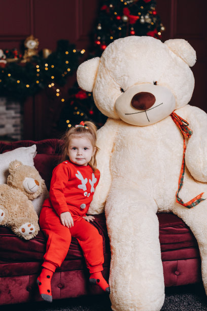 一个小女孩在圣诞树的背景上玩一个大玩具熊图片下载