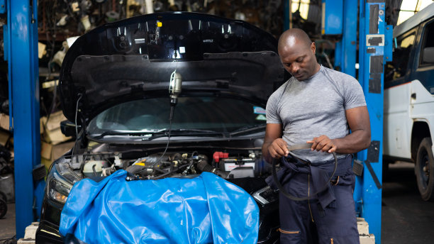 有吸引力的非洲人的肖像微笑的相机和大扳手工具在手中。在汽车修理厂工作的专业技工。图片下载