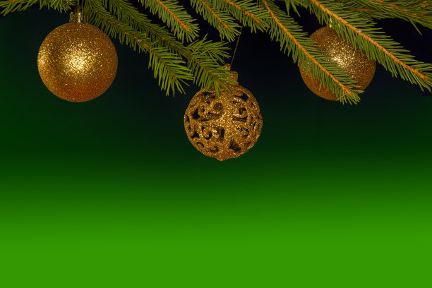 金色的圣诞球挂在绿色背景的圣诞树上。图片下载