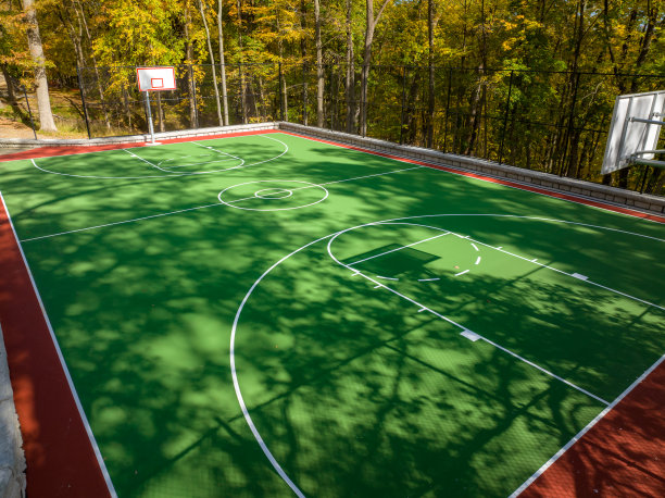 学校操场上绿色和红色的户外篮球场的航拍照片。场地包括挡土墙和黑色乙烯基涂层链环围栏。图片下载